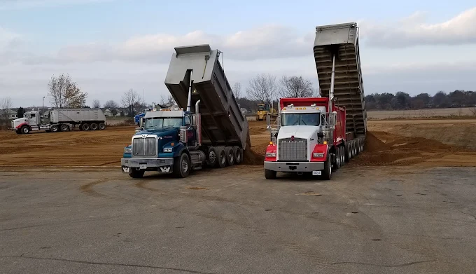 Two dump trucks tipping loads of fill side by side