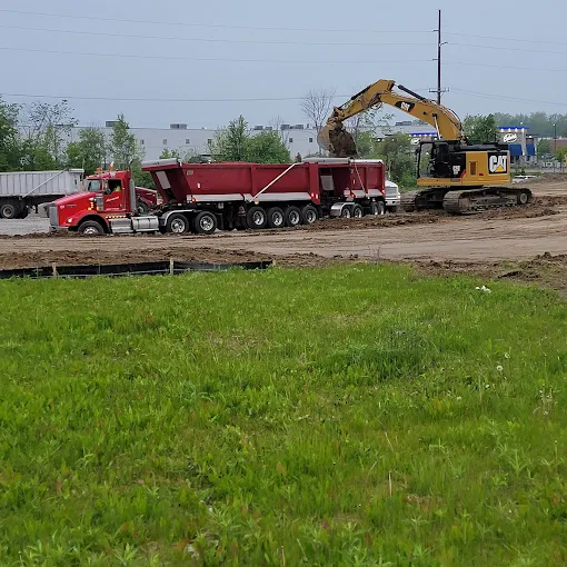 Cat excavator loading a red Kenworth dump train with fill dirt