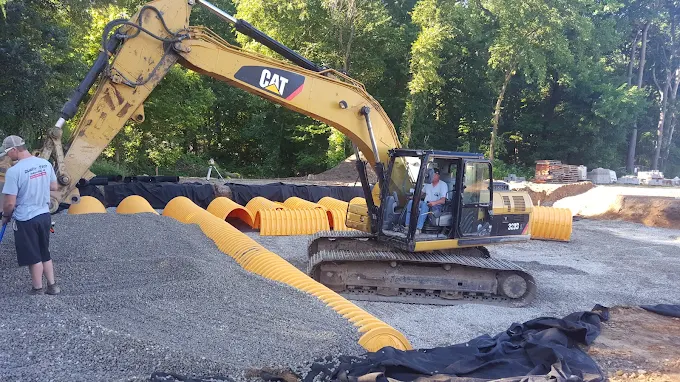 Excavator placing yellow drainage culverts in a gravel bed