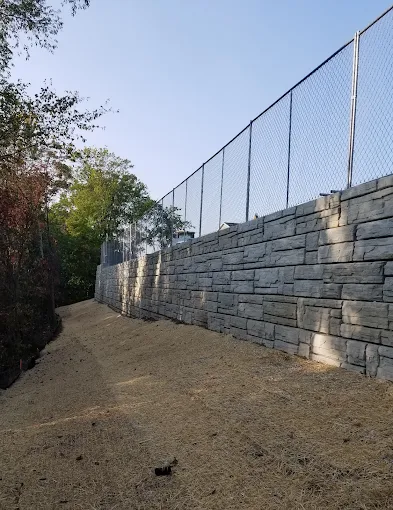 Finished block retaining wall with fence, backfilled and seeded